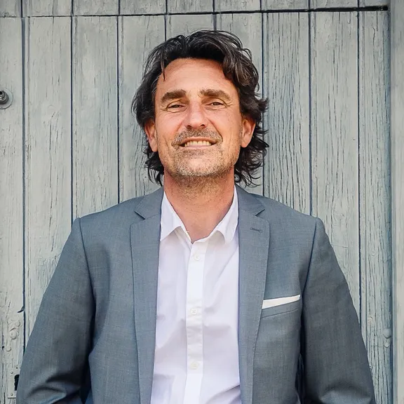 Portrait de Vincent Hermitant, souriant, adossé à une porte en bois patiné bleu-gris